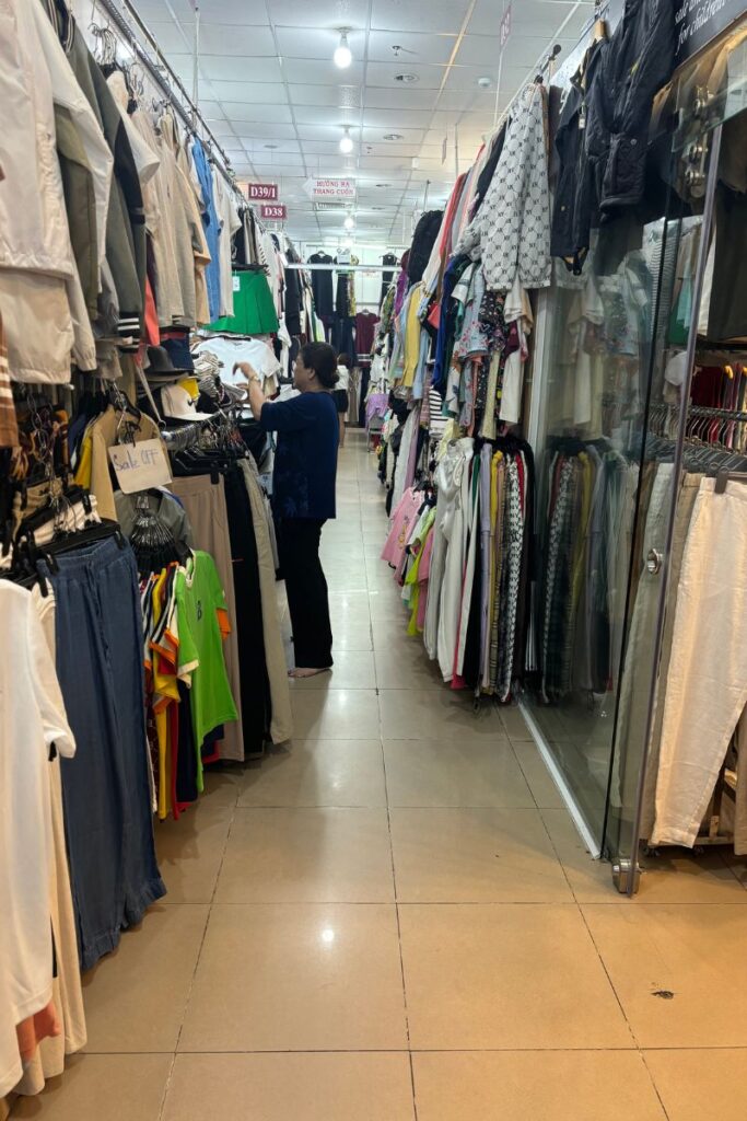 A woman organizes clothes in a busy Vietnam market, where scams in Vietnam like giving incorrect change can sometimes happen.