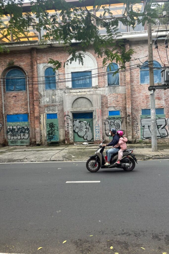 A man and child ride a motorbike past a graffitied building in Ho Chi Minh City, a glimpse of everyday life beyond worries about Vietnamese scams.