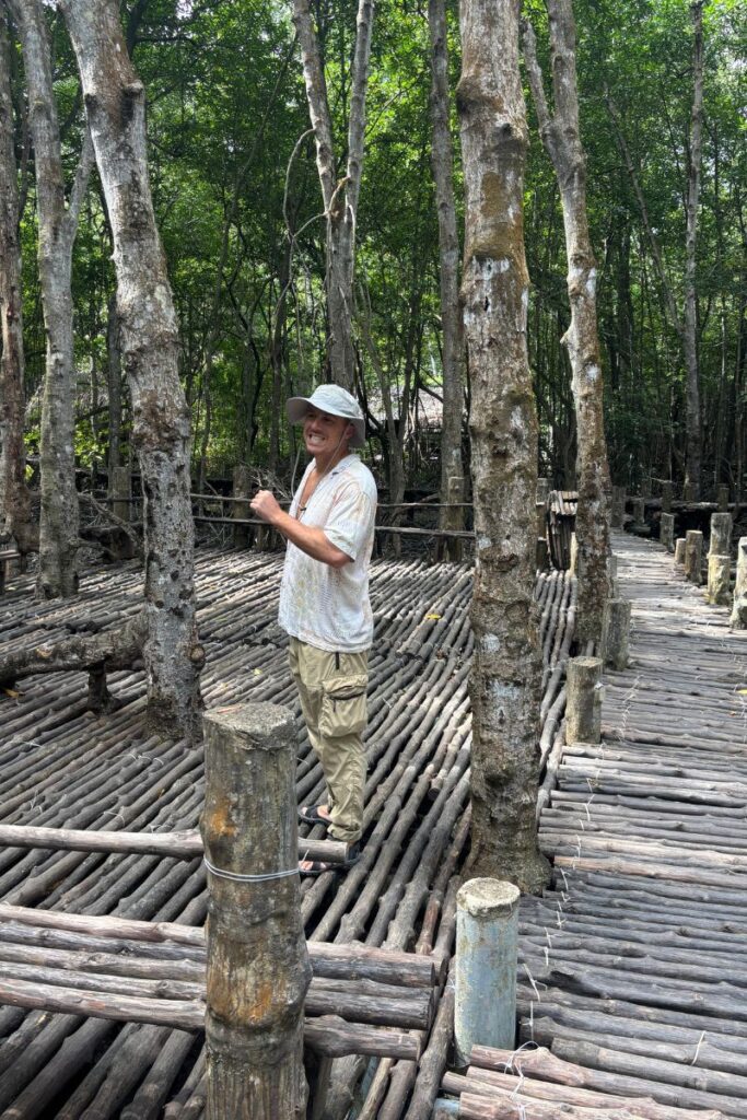 Traveler smiling and posing on a wooden walkway through the mangrove forest at Monkey Island in Can Gio, Vietnam.