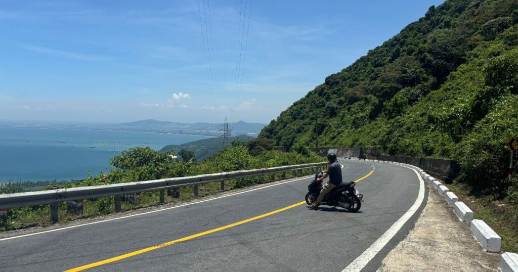 Riding a motorbike along a winding coastal road near Da Nang, Vietnam, a peaceful contrast to the concerns about Vietnamese scams.