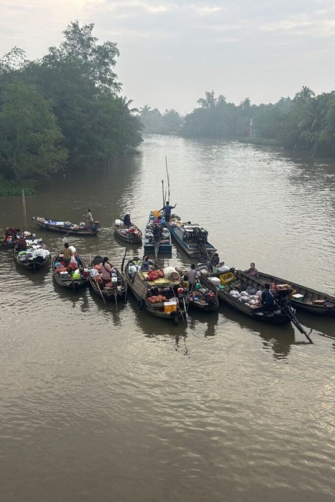 Small boats clustered together at the floating market in Can Tho during the early morning, with vendors selling fresh produce, snacks, and goods directly from their boats on a calm river.