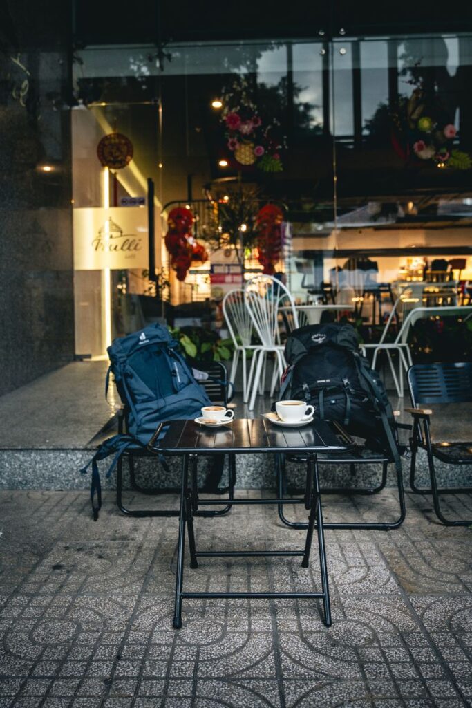 Outdoor coffee shop seating in Ho Chi Minh City with backpacks on chairs, glass walls, and decorative plants, a relaxing stop among Ho Chi Minh City attractions.