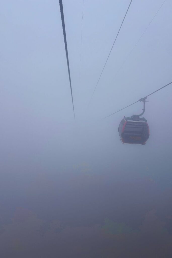 Cable car at Sun World Ba Na Hills suspended in heavy fog, with limited visibility and a single red gondola visible in the frame.