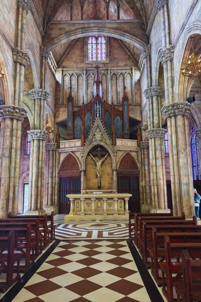 Interior of the cathedral at Ba Na Hills French Village, showing tall stone columns, stained glass windows, and a large pipe organ above a crucifix.