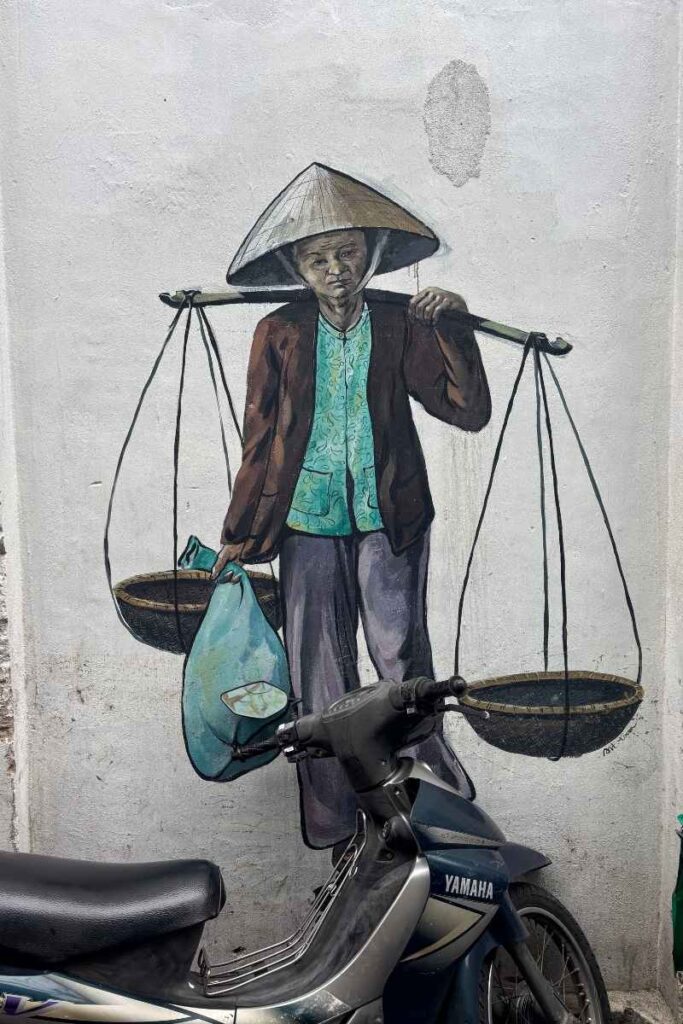A mural in Da Nang’s Fresco Village showing a street vendor carrying baskets on a shoulder pole, capturing everyday Vietnamese life and offering a unique look at what to see in Da Nang beyond the usual spots.