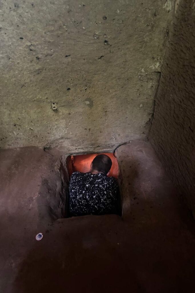 Garrett looking down inside of a tiny tunnel at Cu Chi Tunnels 