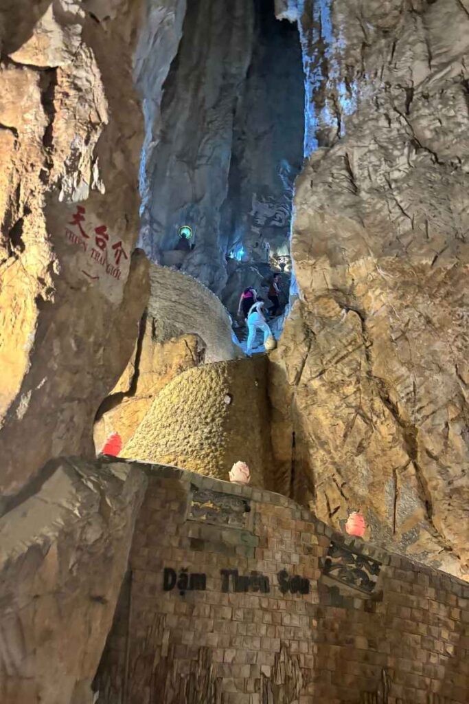 Visitors exploring a cave inside the Marble Mountains in Da Nang, with dramatic rock formations and glowing blue light highlighting one of the top things to see in Da Nang.