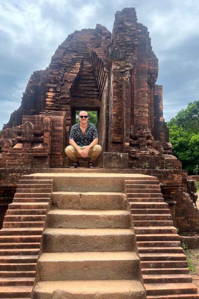 Sitting on temple steps at My Son Sanctuary with ancient brick architecture in the background.