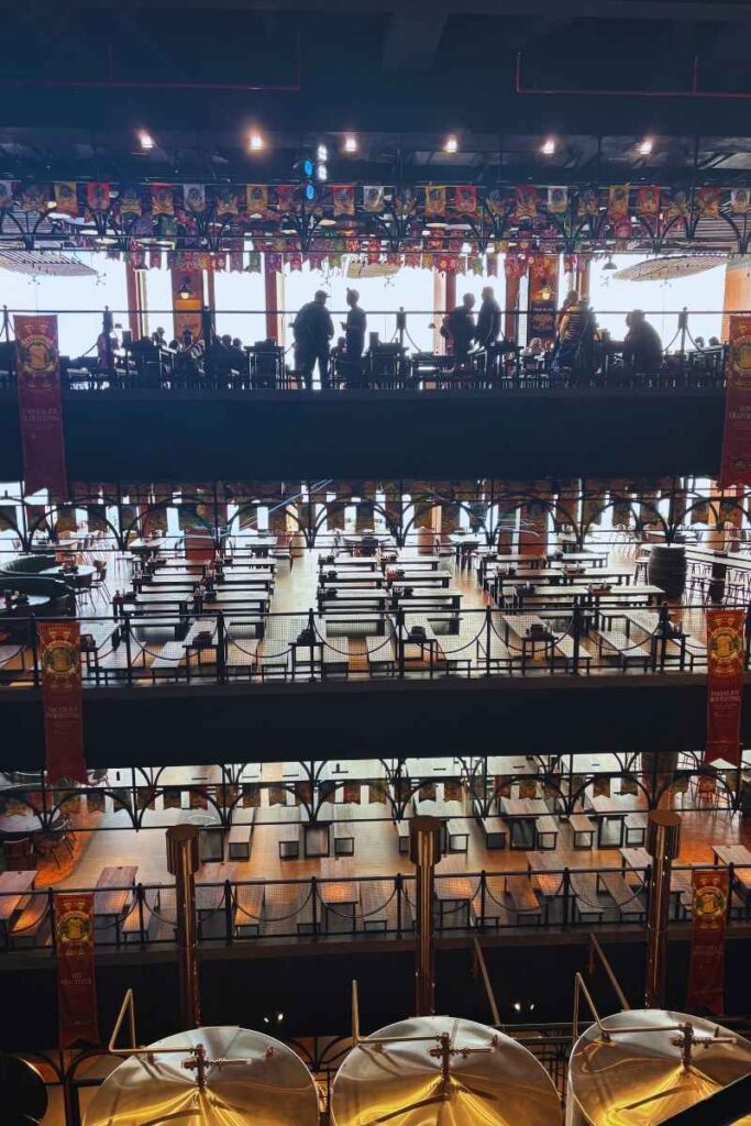 Interior of the Ba Na Hills Brewery showing large brewing tanks in the foreground and multiple levels of dining tables and seating areas in the background.