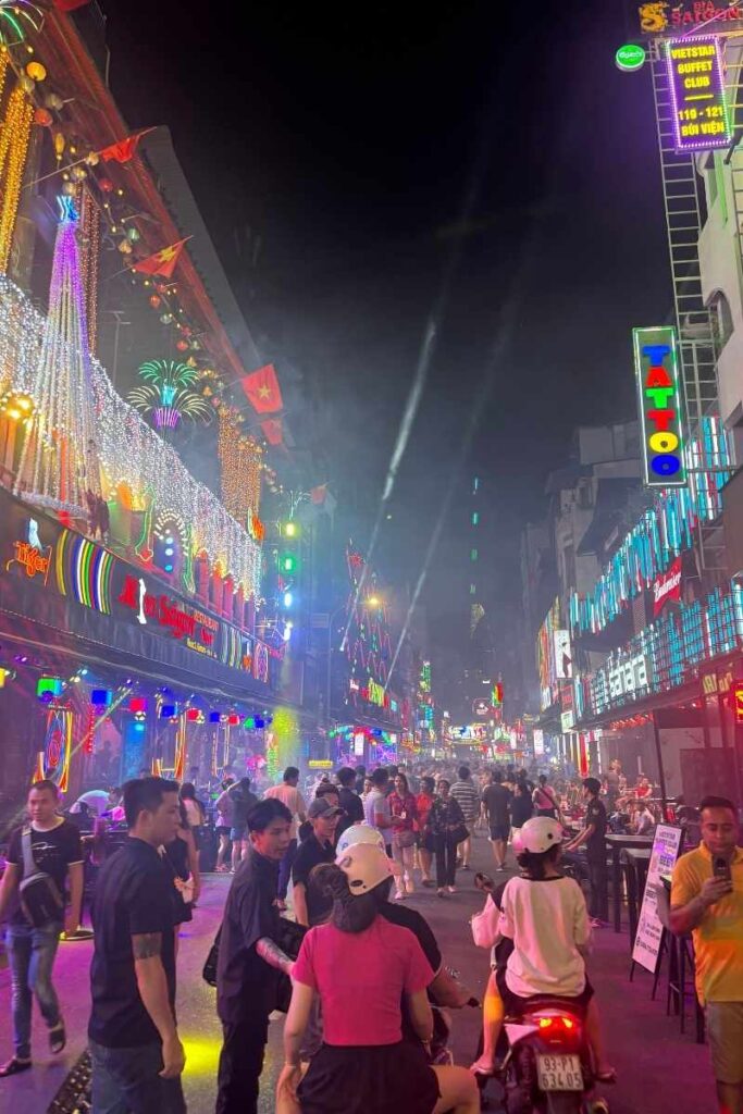 Crowds walking beneath neon lights on Bui Vien Street at night, a popular nightlife hub in Ho Chi Minh City.