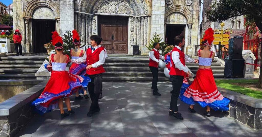 Street performers in red and blue costumes dancing in front of a stone building at Sun World Ba Na Hills.