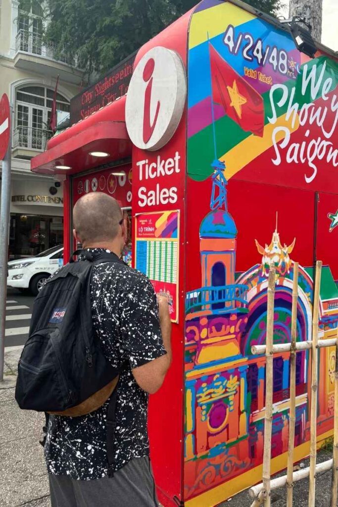 Standing at a bright red ticket booth for the Ho Chi Minh City double-decker bus tour, a fun way to explore things to do in Ho Chi Minh City.