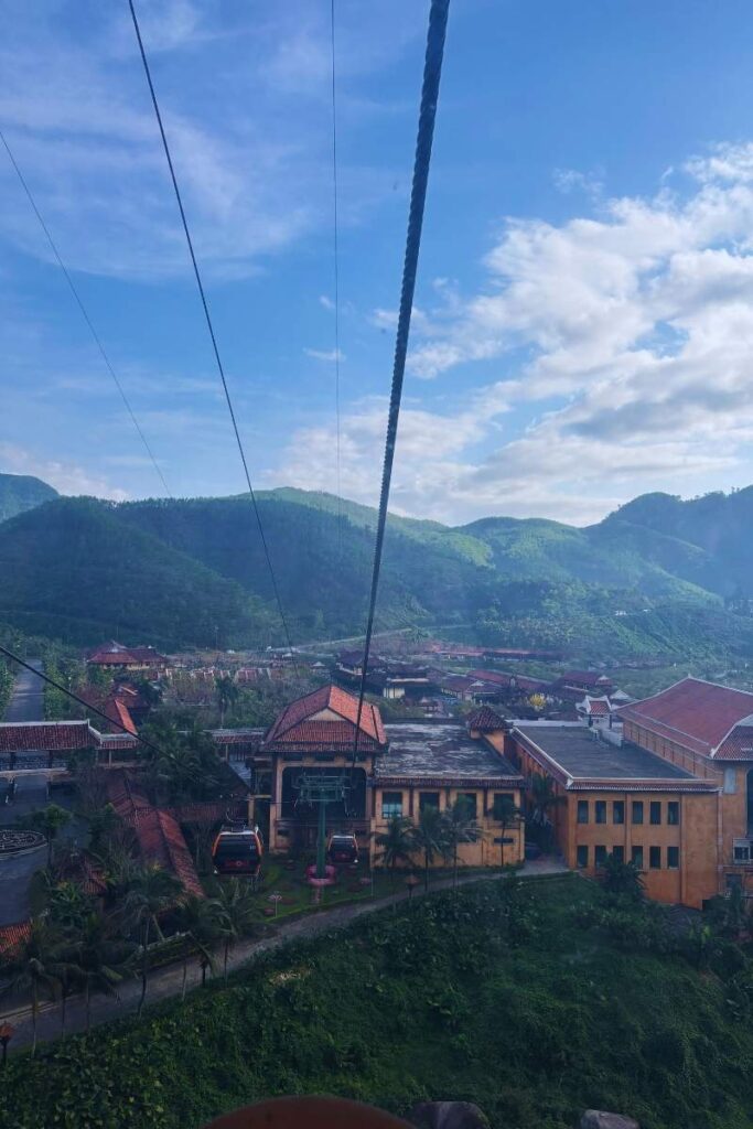 Cable cars arriving at a station at Sun World Ba Na Hills, surrounded by buildings with red-tiled roofs and green mountain scenery in the background.