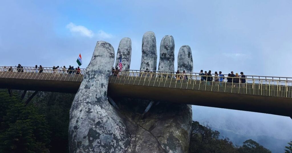 Golden Bridge at Ba Na Hills covered in thick fog, with the giant stone hand sculptures and silhouettes of visitors barely visible.