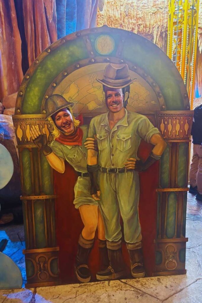 Two people posing with their faces through a cartoon-style explorer cutout board inside Fantasy Park at Ba Na Hills.