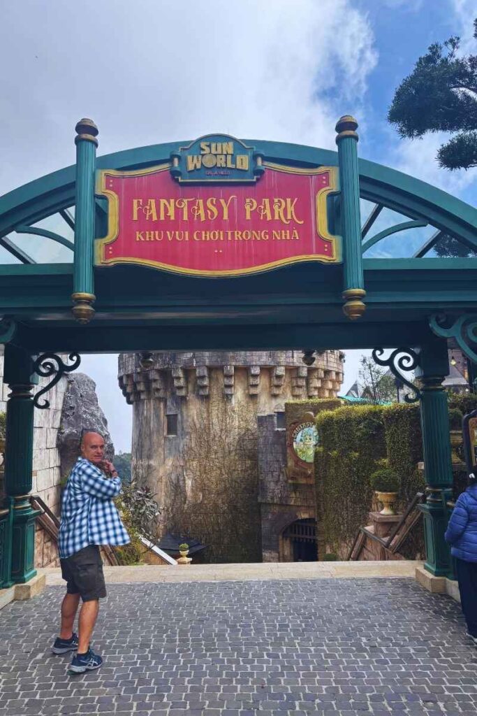 Entrance sign for Fantasy Park at Sun World Ba Na Hills, with a person standing underneath and castle-like structures visible in the background.