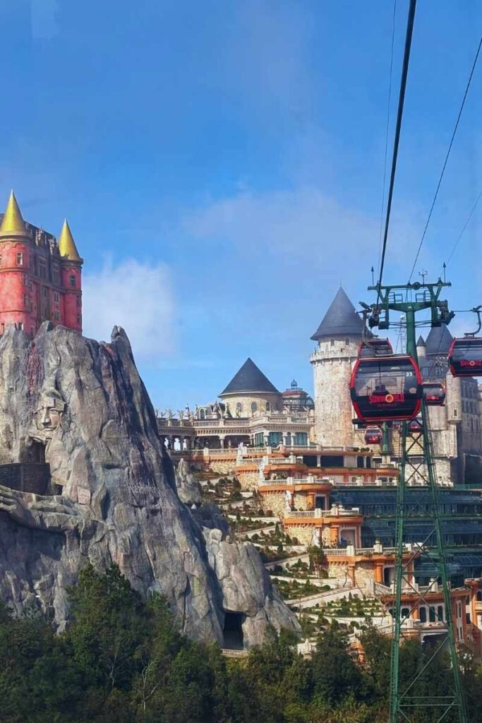 Colorful view of Ba Na Hills with a European-style castle and a cable car gliding up the mountainside under a bright blue sky. The vibrant French Village architecture stands out against lush greenery, showcasing the fantasy atmosphere of Ba Na Hills.