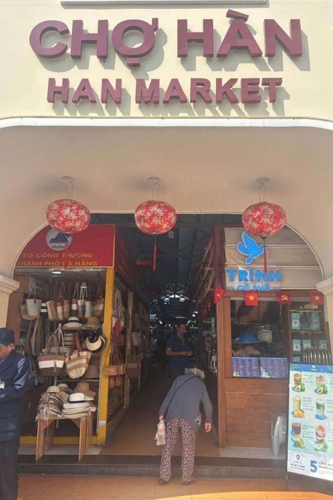 Entrance to Han Market in Da Nang, with shoppers entering under a sign reading “Chợ Hàn” — a popular spot for local goods and a classic Da Nang city activity.