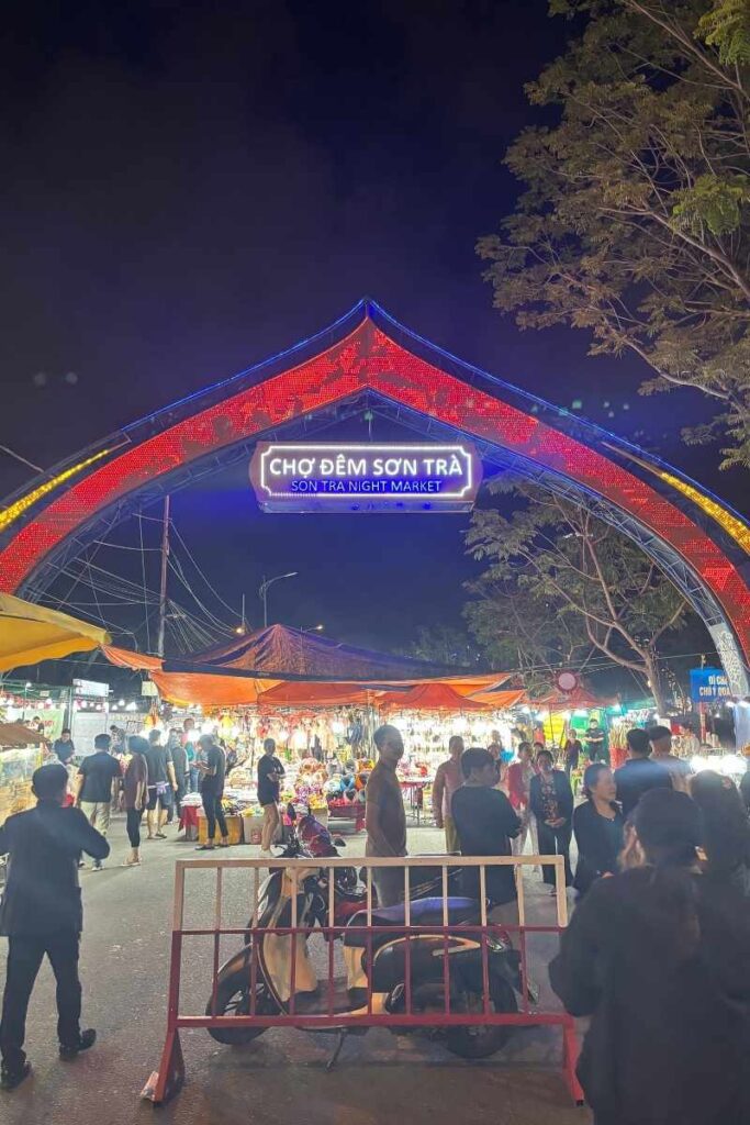 Entrance to Son Tra Night Market in Da Nang lit up with colorful neon lights, as crowds gather to shop, eat, and enjoy one of the best things to do in Da Nang after dark.