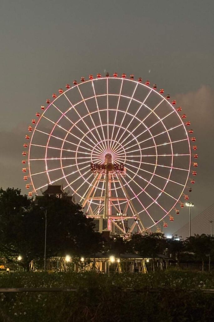The Sun Wheel in Da Nang lit up at night with a dark sky and trees in the foreground.