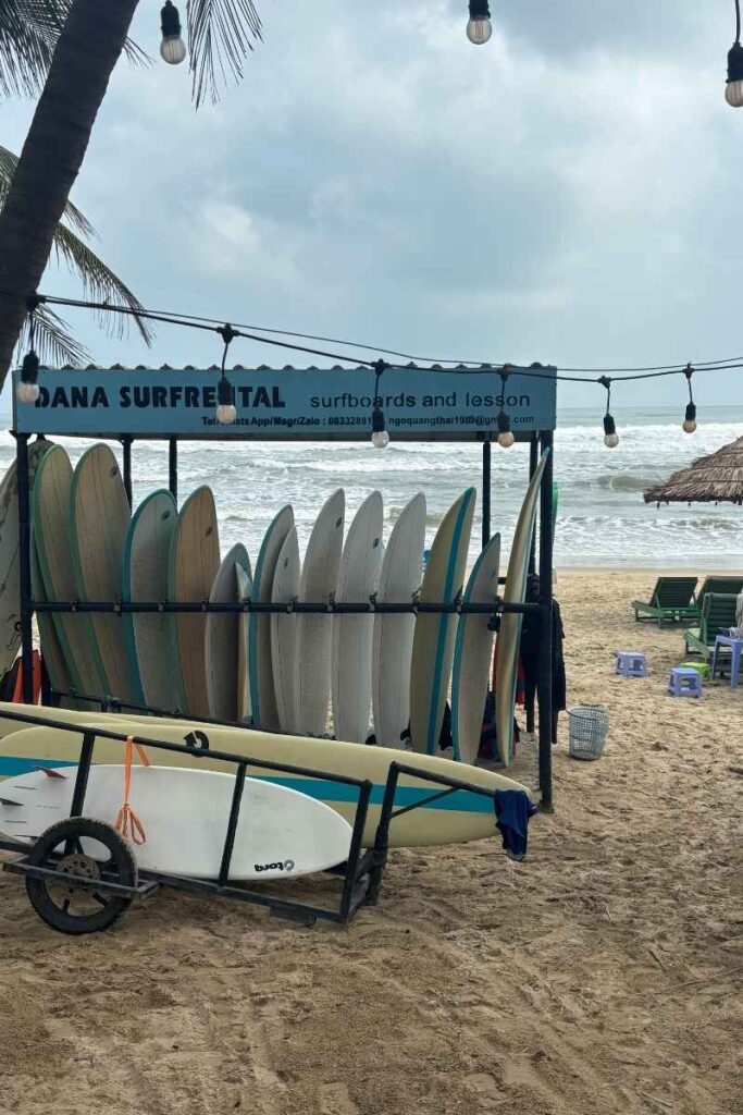 Surfboards lined up on the beach in Da Nang under a shaded rack, ready for lessons or rentals — a laid-back option for travelers looking for active things to do in Da Nang.
