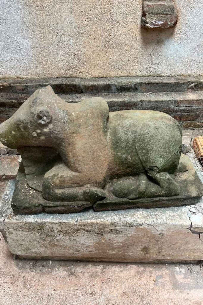 A weathered stone sculpture of a sacred bull (likely Nandi, Shiva’s mount) resting on a platform inside one of the My Son temple structures.