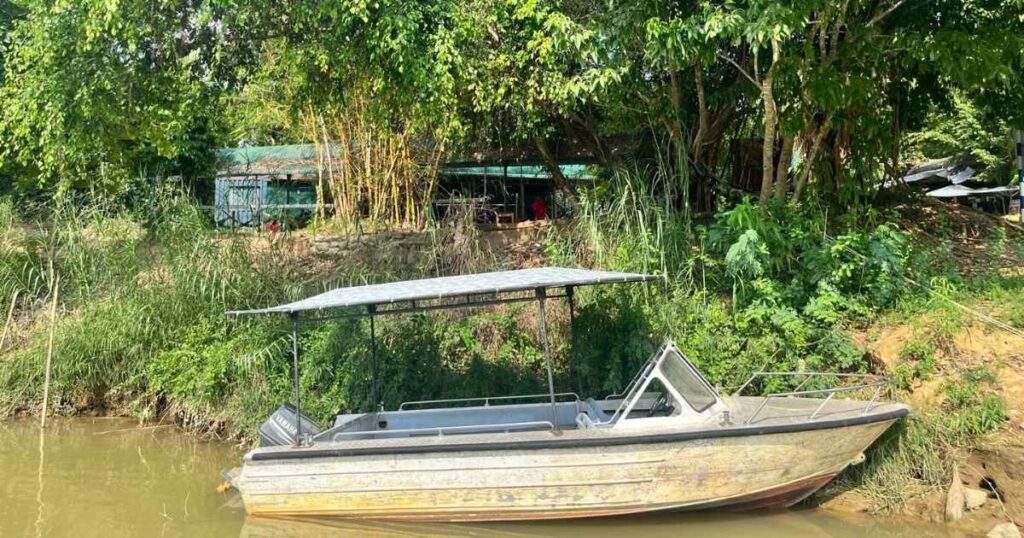 Empty metal boat docked along the forested bank of the Đồng Nai River near Cát Tiên, a popular option for wildlife boat tours.