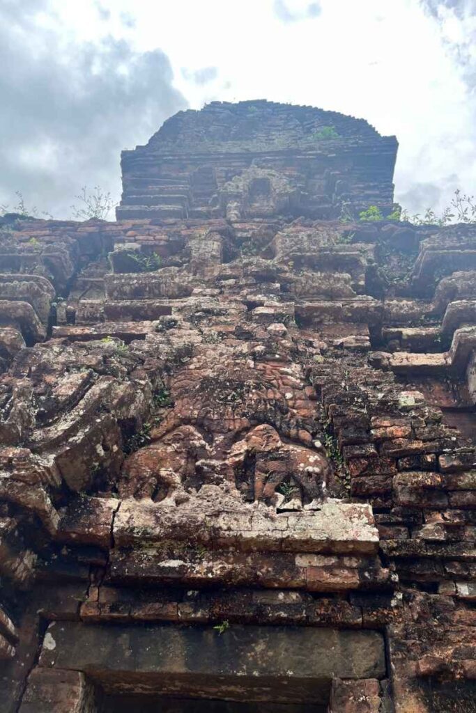 Upward view of an ancient brick tower at My Son Sanctuary with weathered carvings, including elephants and mythical creatures.