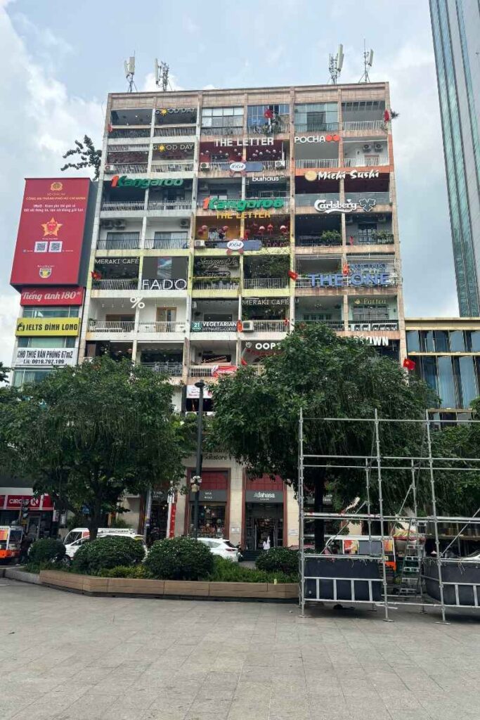 Facade of the Café Apartment building in Ho Chi Minh City, filled with colorful signs for coffee shops, sushi bars, and boutiques stacked across multiple floors.