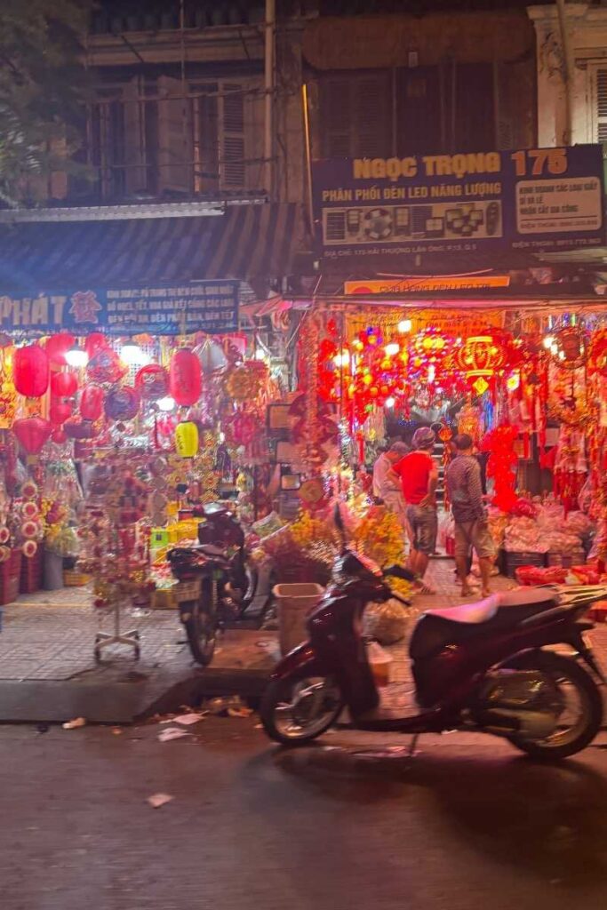 Bustling Tet market in Ho Chi Minh City at night, filled with glowing red lanterns, decorative goods, and shoppers browsing stalls packed with holiday items.