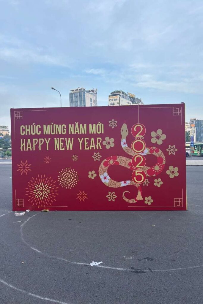 Bold red Tet sign in Ho Chi Minh City with golden text reading "Chúc Mừng Năm Mới" and "Happy New Year," featuring a stylized snake for the 2025 Lunar New Year.